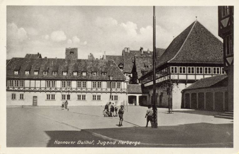 Foto-Postkarte: Ballhofplatz. Die Postkarte zeigt eine Fotografie des Ballhofplatzes mit Blickrichtung Nordost. Die Dächer im Hintergund lassen darauf schließen, dass die Aufnahme vor der Zerstörung im 2. Weltkrieg getätigt wurde. 1938-1945